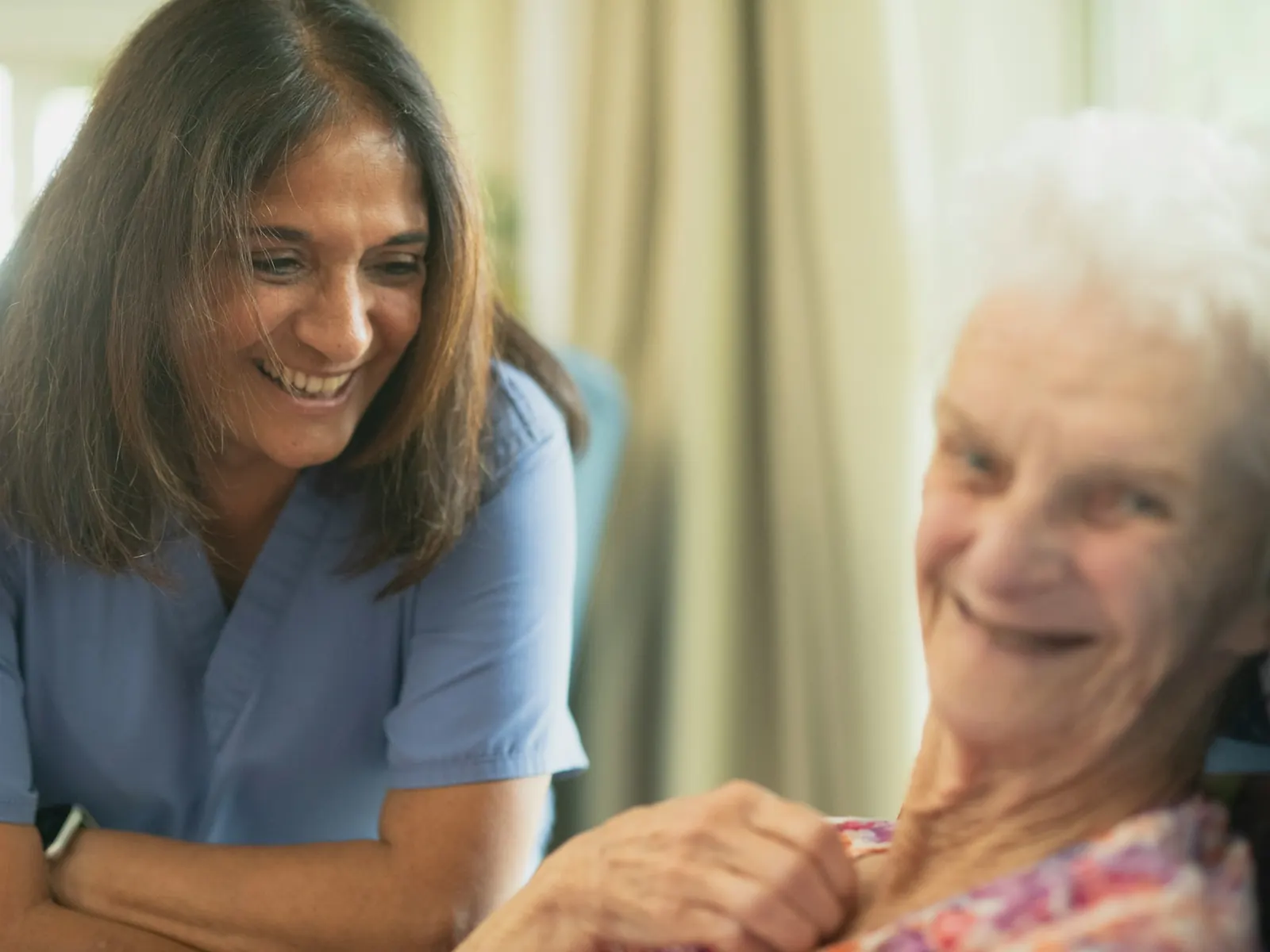 Mujer con uniforme azul sonriendo junto a una señora mayor que también sonríe