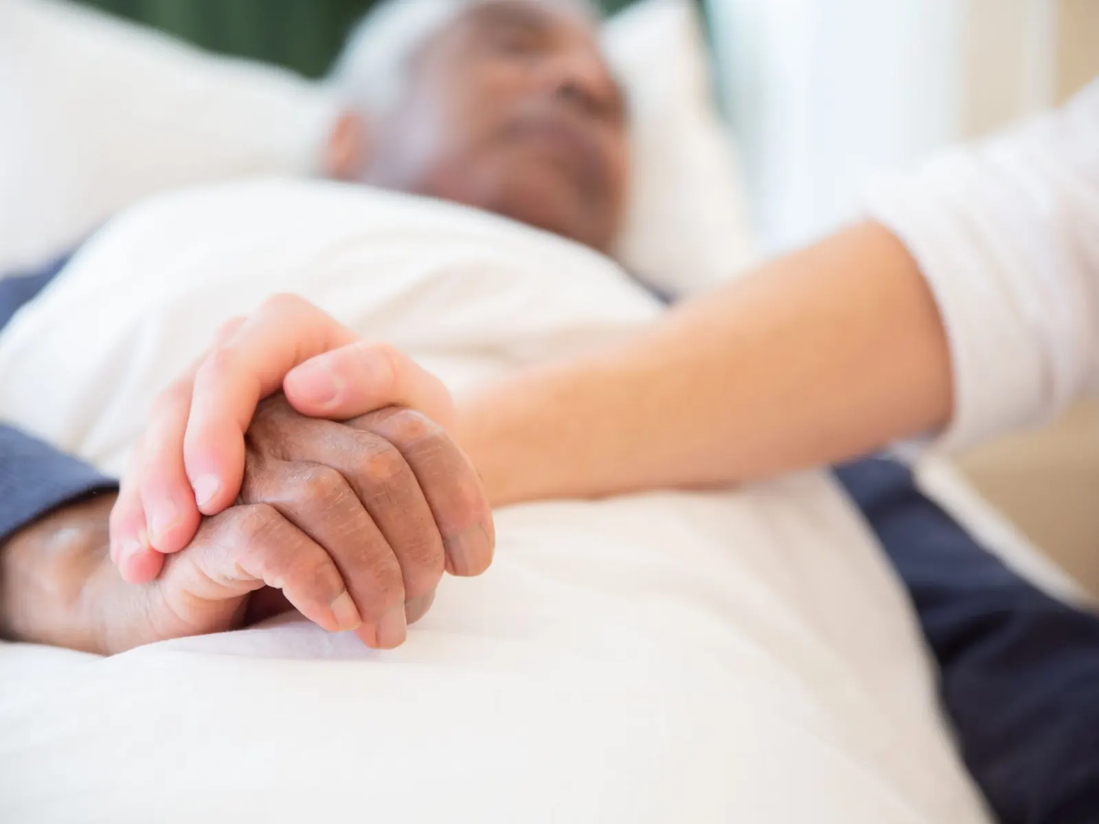 Una mano sujeta la de un hombre mayor tumbado en una cama de hospital