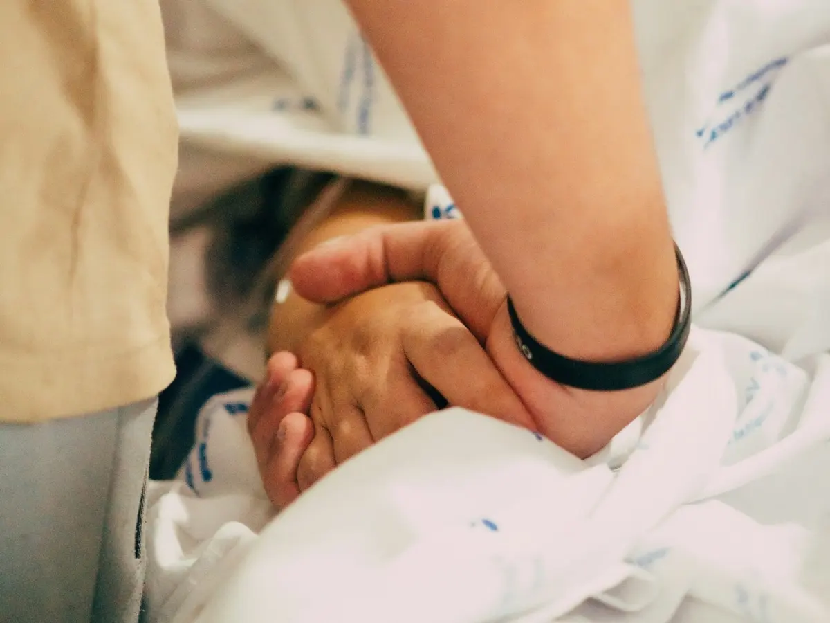 Una mano coge la de un paciente sobre las sábanas de una cama de hospital