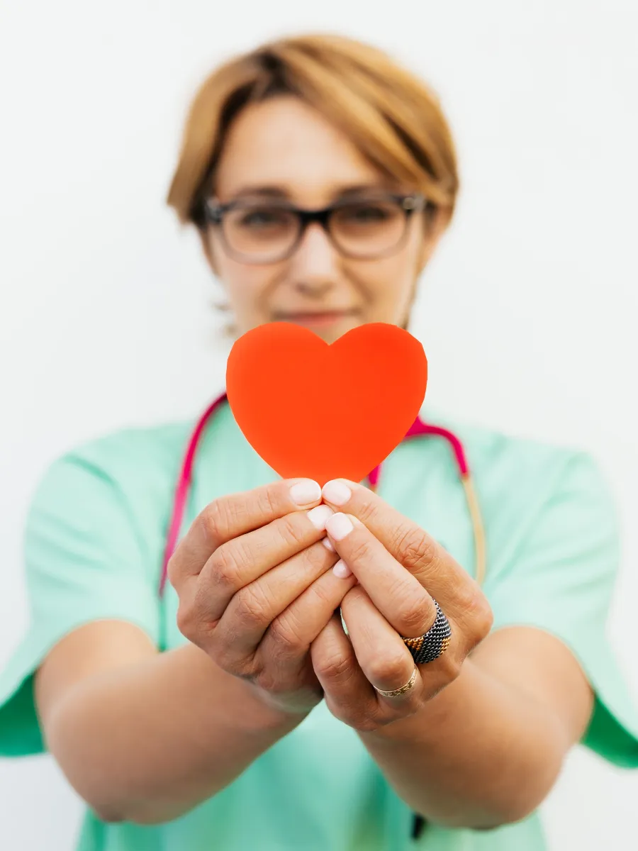 Profesional sanitaria con bata verde sosteniendo un corazón de papel entre las manos