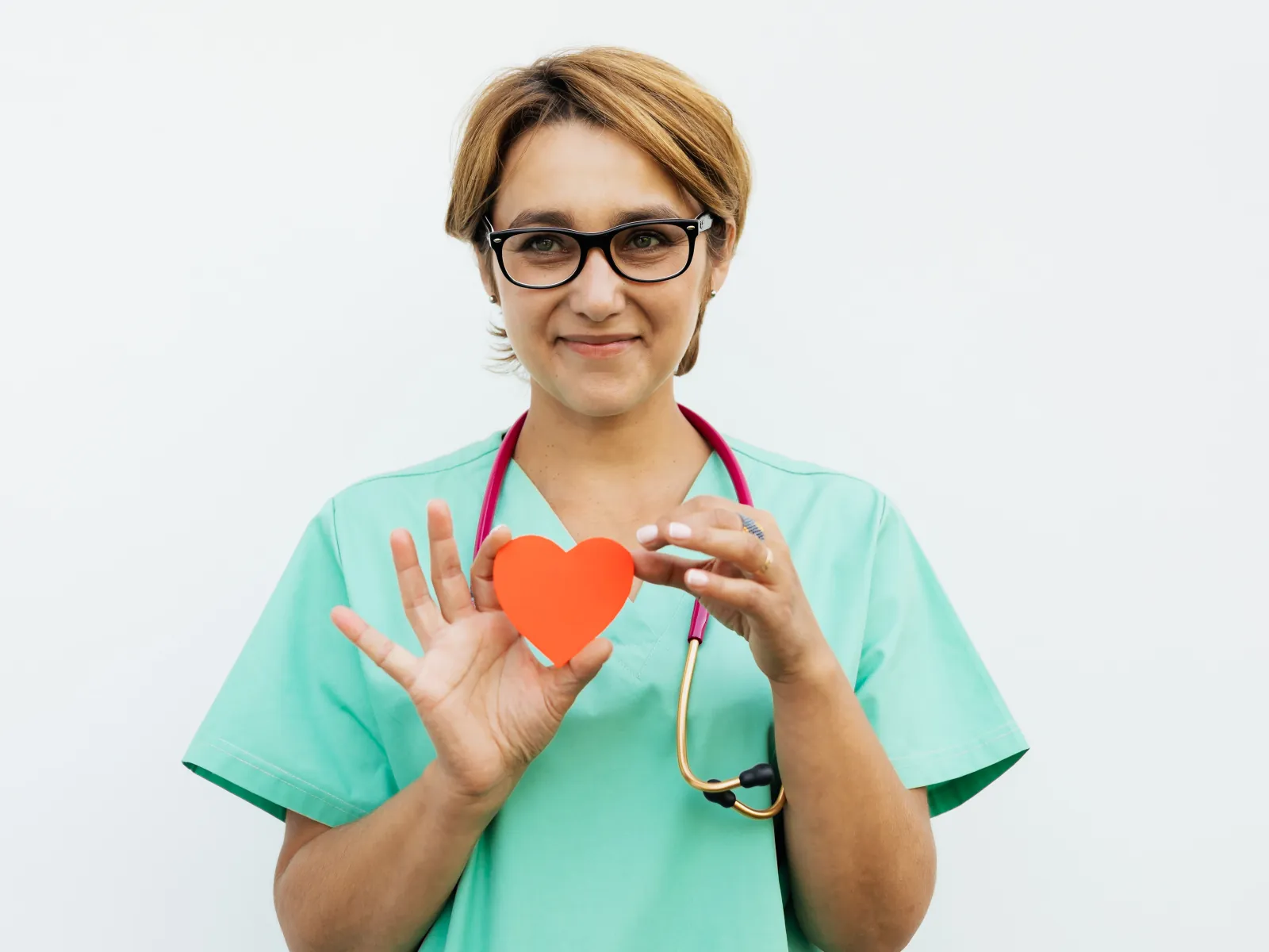 Profesional con uniforme verde sujetando un corazón de papel naranja con las dos manos a la altura del pecho