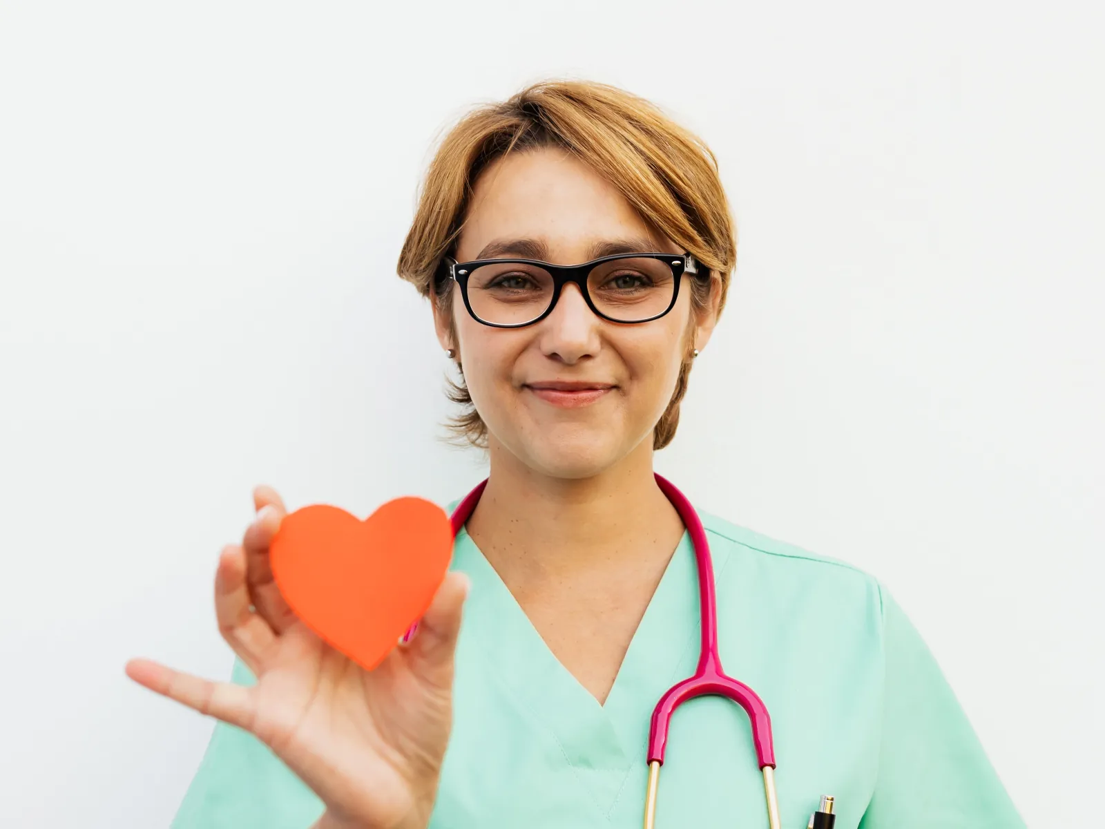 Enfermera con gafas sosteniendo un corazón de papel naranja sobre la palma de la mano
