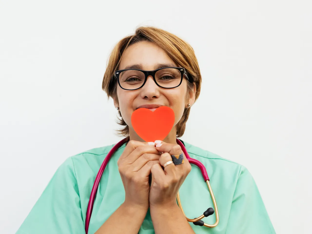 Profesional sonriente sujetando un corazón de papel coral junto al rostro
