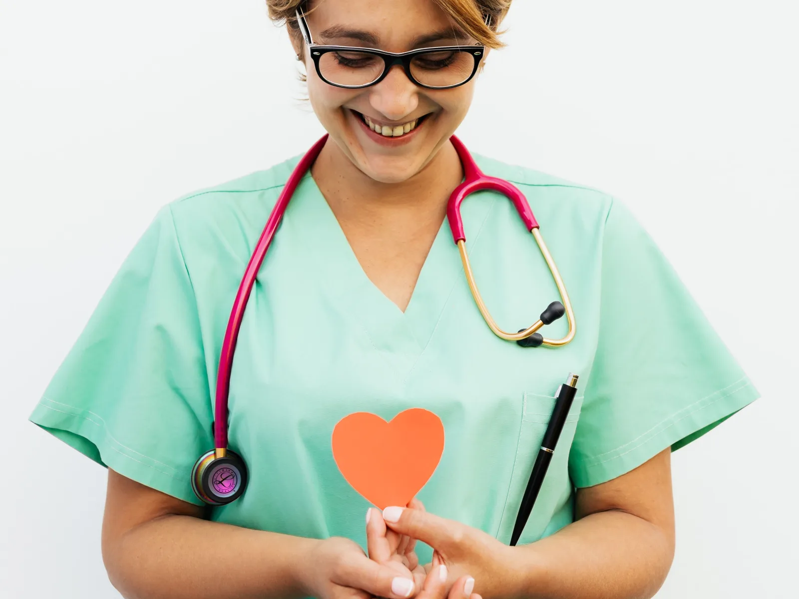 Profesional con uniforme sanitario sonriendo mientras sostiene un corazón de papel naranja con las dos manos